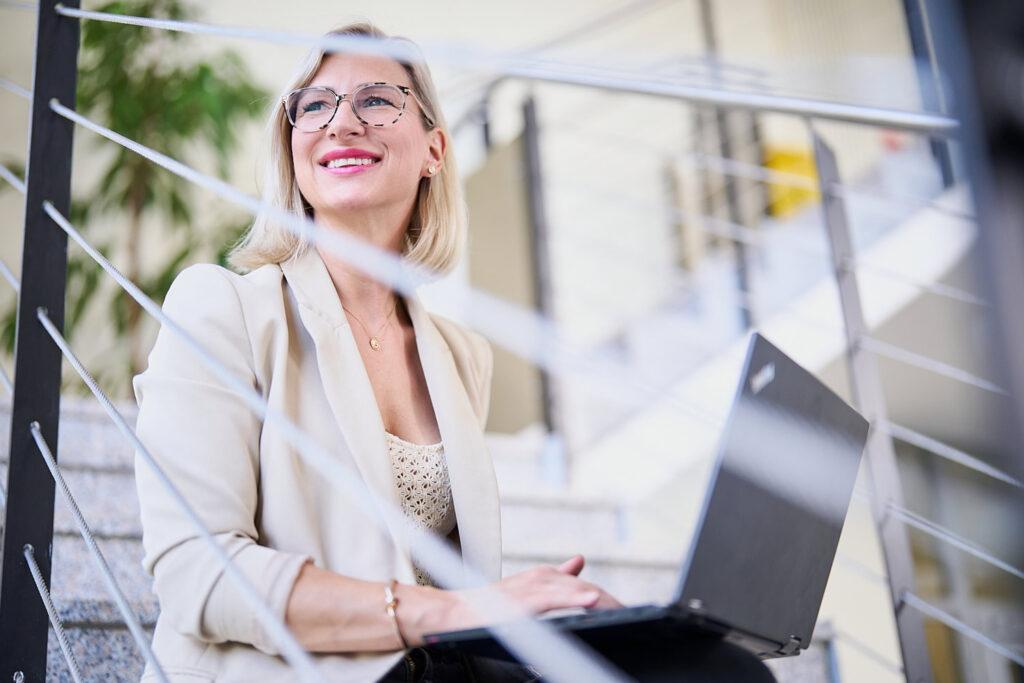 Mitarbeiterin mit Laptop lächelt und schaut aus dem fenster